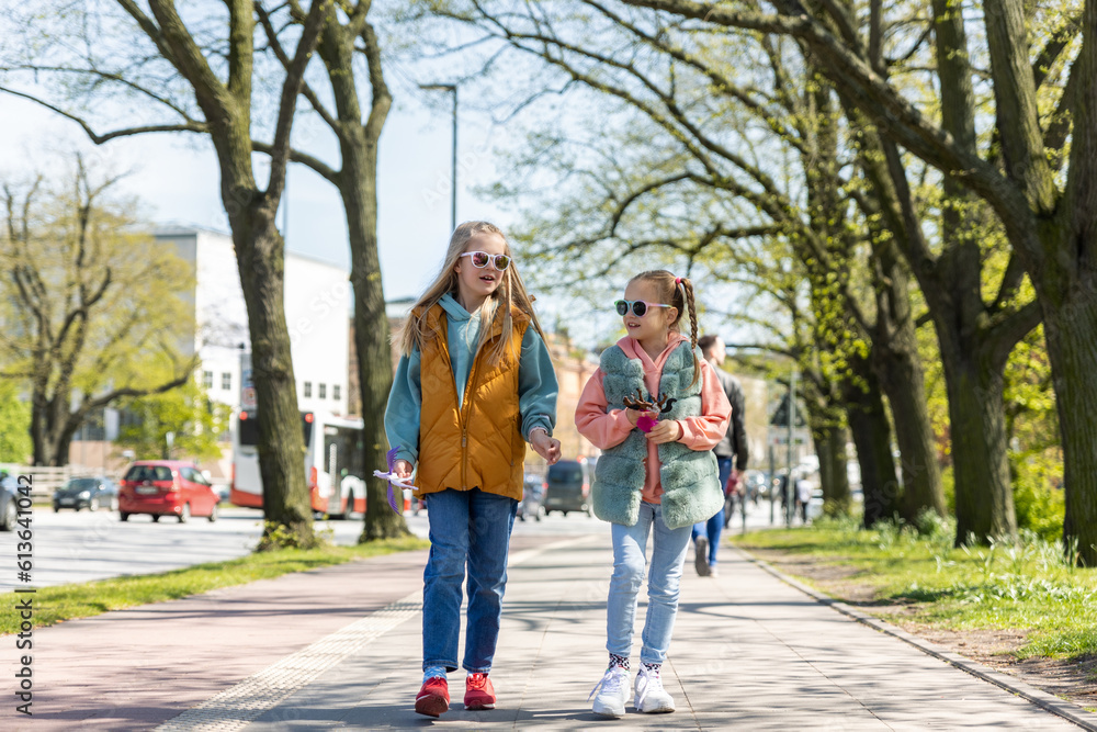 Two cute little children girlfriends enjoy fun talk walking in Hamburg city street park on sunny day outdoors. Happy small friends portrait wear sunglasses. Portrait of pair stylish kids outside