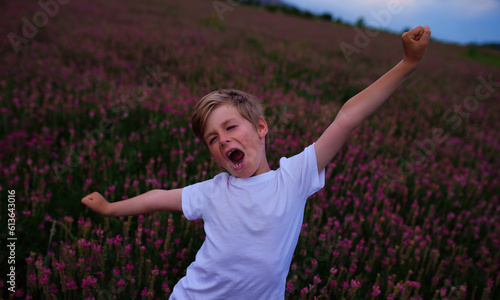 Happy boy stretching in flower meadow at twilight
