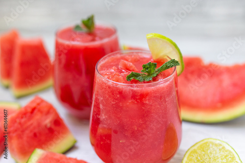 Watermelon smoothies with slices of fruit and leaf of mint and lime over white wooden background.