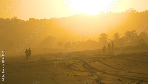 Silhouettes of unrecognizable people walking on misty sandbeach in golden light