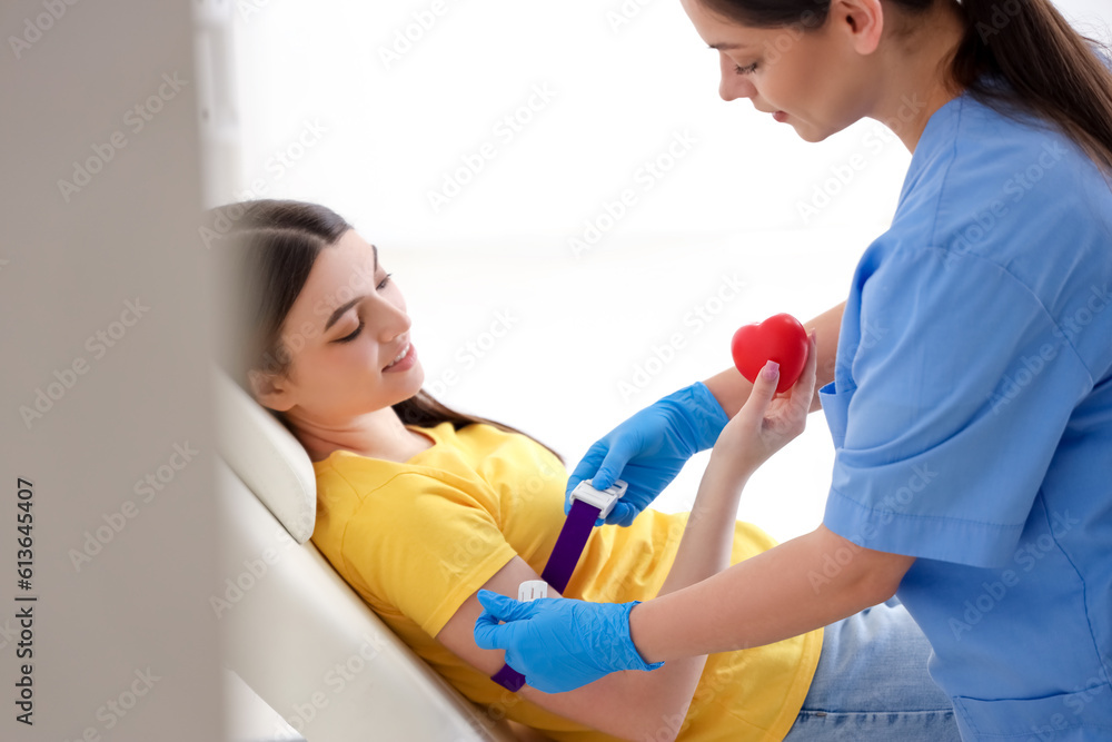 Female nurse preparing young donor for blood transfusion in clinic Female nurse preparing young donor for blood transfusion in clinic