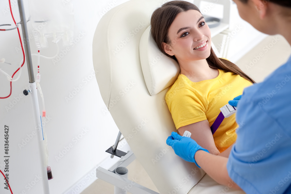 Female nurse preparing young donor for blood transfusion in clinic Female nurse preparing young donor for blood transfusion in clinic