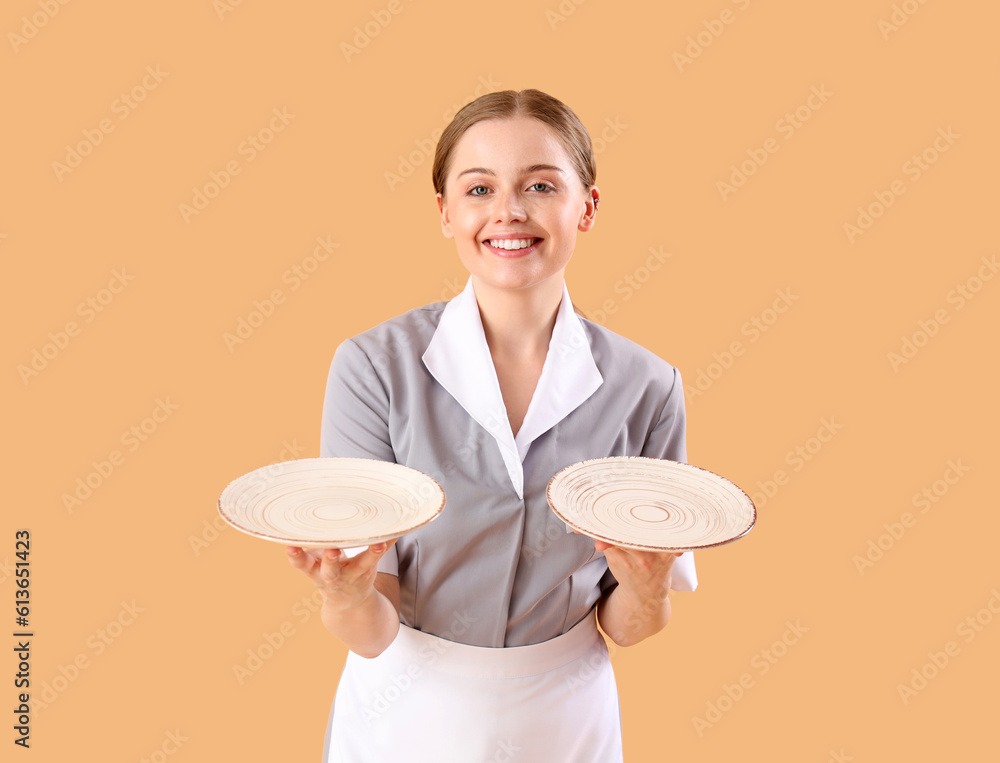 Beautiful young waitress with empty plates on beige background Beautiful young waitress with empty plates on beige background