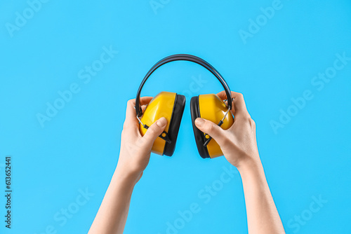 Photography Female hands holding ear muffs on blue background