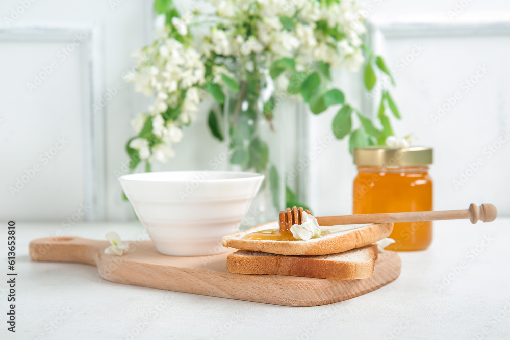 Bowl of honey with flowers of acacia and toasts on light background