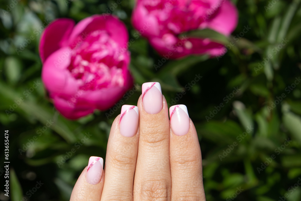 Beautiful female hand with pink manicure nails on peonies flower background Beautiful female hand with pink manicure nails on peonies flower background