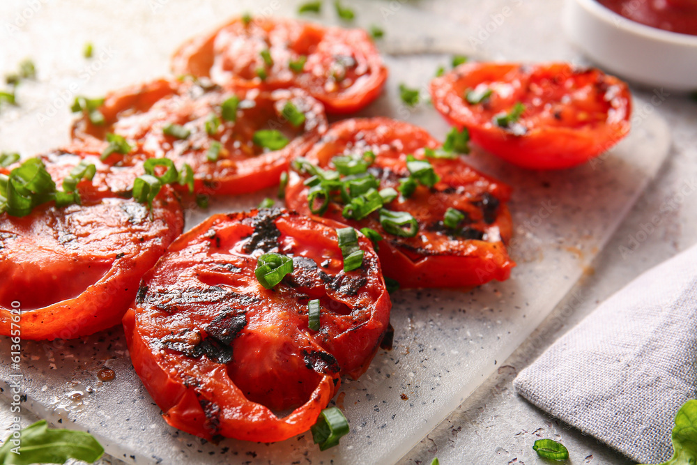 Board with tasty grilled tomatoes and green onion on grey background