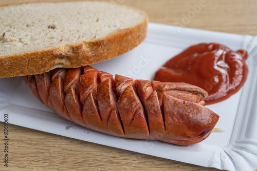 Close-up of sliced ​​sausage with bread and ketchup on a paper tray.