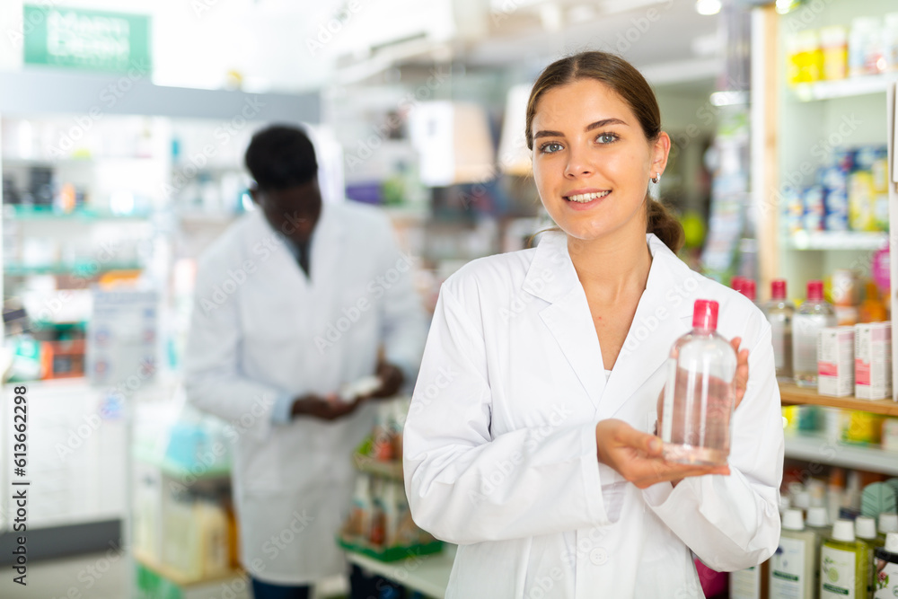 Female pharmacist in gown demonstrating skin care product in salesroom of drugstore