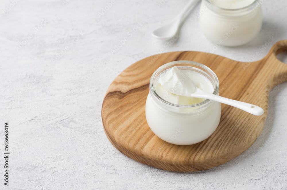 Natural homemade yogurt in a glass jar on a wooden board on a light gray background Natural homemade yogurt in a glass jar on a wooden board on a light gray background