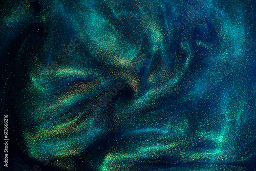 Abstract magic blue background with golden sparkles. Photo of a blue liquid with gold glitters and green tints. Various shades of green and blue with golden splashes and flows. 