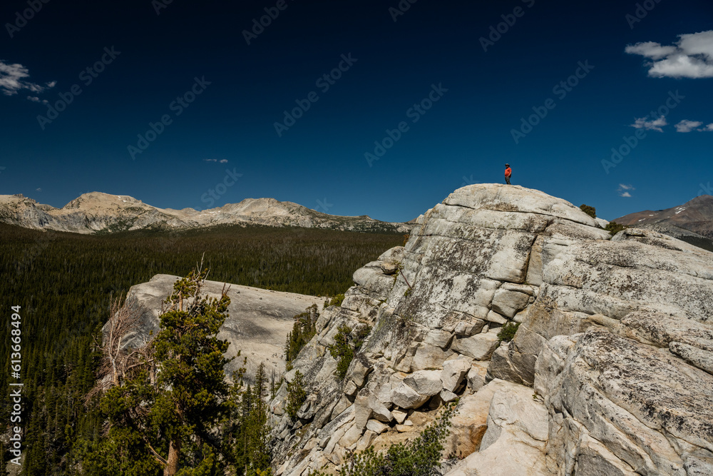 Hiker In Orange Shirt Stands Atop Lembert Dome and Looks Out Over Tuolumne Meadows