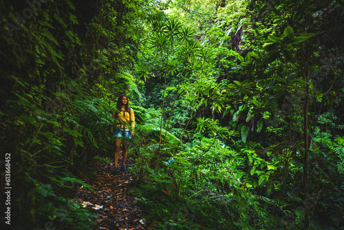Backpacker woman walks through Madeiran rainforest on overgrown hiking trail in the morning. Levada of Caldeirão Verde, Madeira Island, Portugal, Europe.