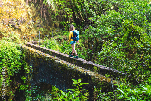 Backpacker woman walking on overgrown footpath over old bridge in Madeira's rainforest in the morning. Levada of Caldeirão Verde, Madeira Island, Portugal, Europe.