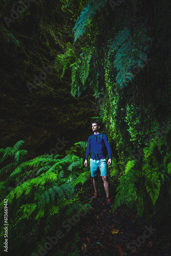 Atlhletic backpacker man walking on a fern covered gorge with old bridge somewhere in Madeiran rainforest in the morning. Levada of Caldeirão Verde, Madeira Island, Portugal, Europe.