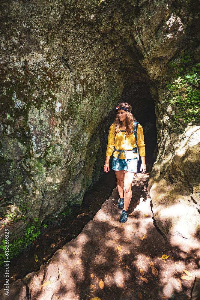 Tourist woman exiting a tunnel along an overgrown jungle trail next to a canal in Madeira rainforest. Levada of Caldeirão Verde, Madeira Island, Portugal, Europe. Tourist woman exiting a tunnel along an overgrown jungle trail next to a canal in Madeira rainforest. Levada of Caldeirão Verde, Madeira Island, Portugal, Europe.