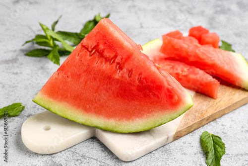 Board with pieces of fresh watermelon and mint on grey background