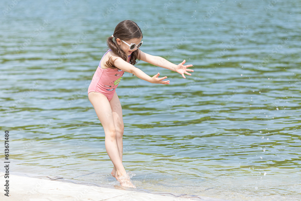 Naklejka premium Little girl playing on the beach on summer holidays. Child having fun with a sand on the city lake seashore. Vacation concept. Happy sunny day
