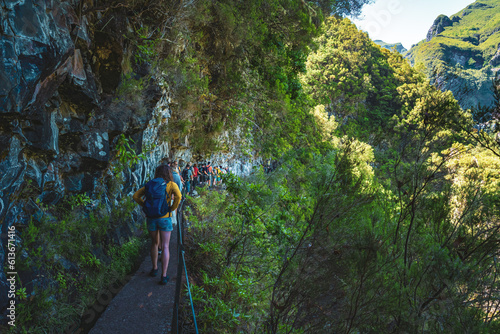 Tourist group walking along steep cliff jungle hiking trail  next to canal through Madeiran rainforest. Levada of Caldeirão Verde, Madeira Island, Portugal, Europe. photo