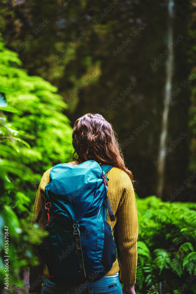 Backpacker woman on a fern covered path overlooking a picturesque overgrown waterfall in Madeiran rainforest. Levada of Caldeirão Verde, Madeira Island, Portugal, Europe. Backpacker woman on a fern covered path overlooking a picturesque overgrown waterfall in Madeiran rainforest. Levada of Caldeirão Verde, Madeira Island, Portugal, Europe.