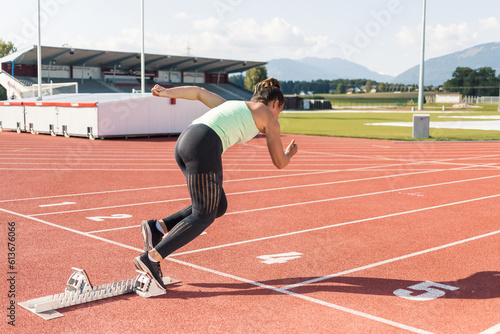 Young woman preparing for the run race, taking a start position for sprint, using starting block
