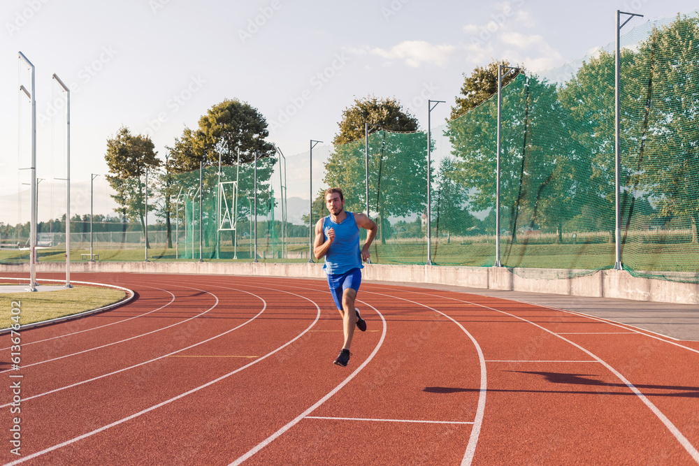 Obraz premium Caucasian male athlete in blue sportswear running alone along an athletic track on the stadium
