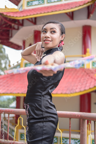 A young Asian woman wears a black dress while holding a hand fan