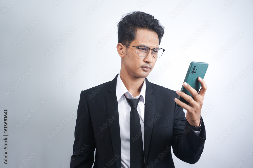 Portrait of a young cheerful excited asian man wearing suit standing isolated over white background, using mobile phone Portrait of a young cheerful excited asian man wearing suit standing isolated over white background, using mobile phone