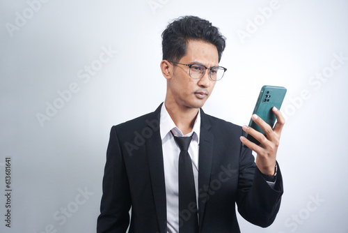 Portrait of a young cheerful excited asian man wearing suit standing isolated over white background, using mobile phone