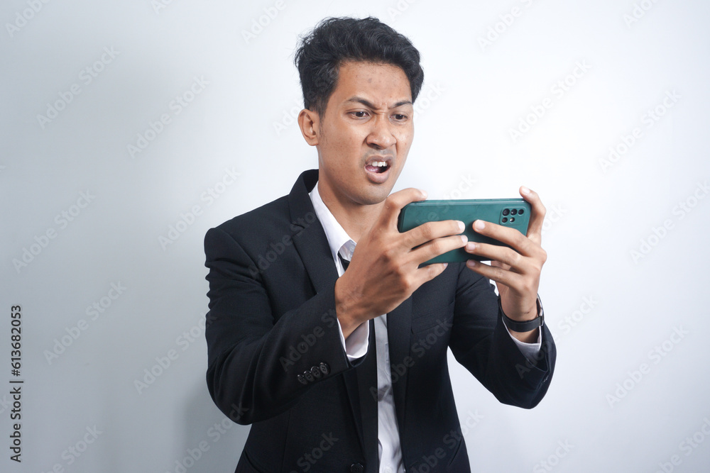 Angry Asian young man get mad on the smartphone when play game at work. Indonesian man wearing suit. Angry Asian young man get mad on the smartphone when play game at work. Indonesian man wearing suit.