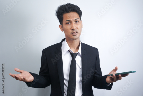 pose of asian man shrugging both shoulders and raising both hands. illustrations of ignorance, why not, where, and what's wrong. portrait of Indonesian man on isolated white background