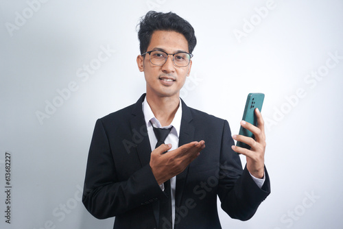 Portrait of a happy Asian young man wearing a suit while pointing at a mobile phone © AriaSandi