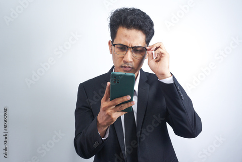 Portrait of handsome young adult with dreamy look, thinking while holding smartphone, isolated over white background.