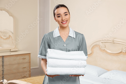 Young chambermaid holding stack of clean towels in hotel room photo