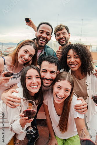 Vertical portrait. Group of best friends on a rooftop wine party. Young people drinking, toasting glasses, laughing and having fun on a friendly meeting, enjoying happy hour at winery bar restaurant