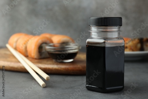 Tasty soy sauce, chopsticks and sushi rolls with salmon on grey table. Space for text