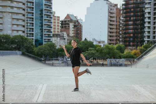 general shot of a teenage girl looking at the camera, smiling, with a funny pose in the middle of the city