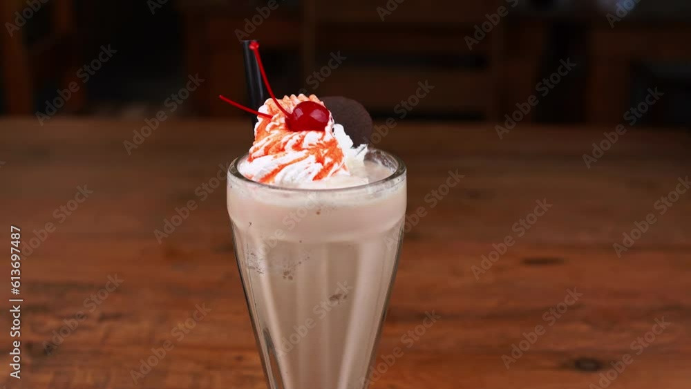 Detailed close up of chocolate milkshake, with caramel, espresso coffee and whipped cream with cherry, hand taking whipped cream with a chocolate cookie and ice cream with caramel Detailed close up of chocolate milkshake, with caramel, espresso coffee and whipped cream with cherry, hand taking whipped cream with a chocolate cookie and ice cream with caramel