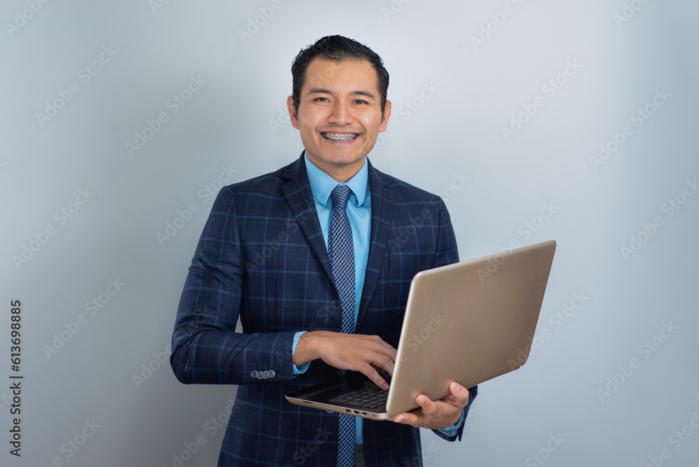 Young man with brown skin smiles dressed as a businessman with a laptop, blue clothes Young man with brown skin smiles dressed as a businessman with a laptop, blue clothes