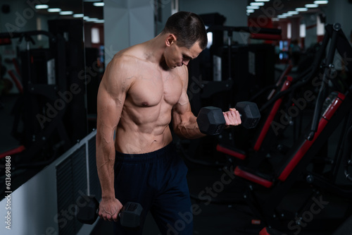 Shirtless man doing bicep exercises with dumbbells in the gym. 