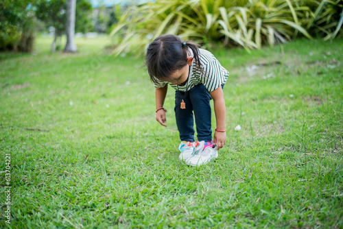 Asian girl bends down to put on shoes by herself in the backyard while doing mom and dad family vacation activities.