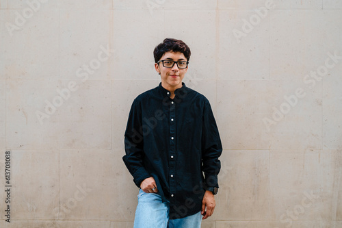 Young transgender man leaning on a wall while posing outdoors on the street.
