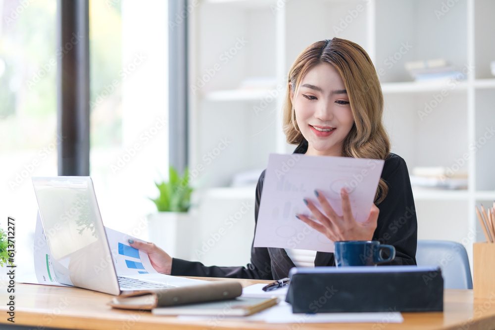 Professional woman analyst wearing suit sitting at officedesk, using laptop and and reading statistics report. Professional woman analyst wearing suit sitting at officedesk, using laptop and and reading statistics report.