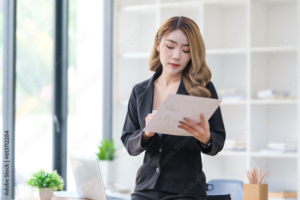 Gorgeous businesswoman standing at desk in office and reading statistics report. Gorgeous businesswoman standing at desk in office and reading statistics report.