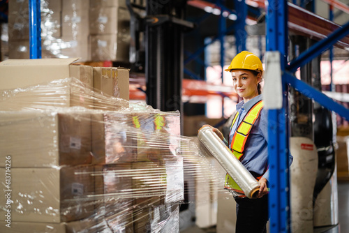 Bilde på lerret Female worker wrapped a parcel of stretch film on a cargo in a large factory warehouse