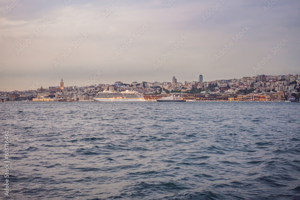 Huge cruise ship docked at terminal of Galataport, located along shore of Bosphorus strait, in Karakoy neighbourhood, with Galata tower in the background
