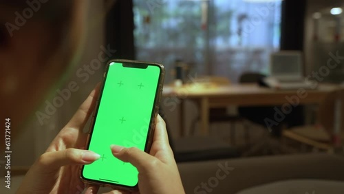 Person living room holding in hands a smartphone with green screen chroma mock up over a comfy blurred living room background