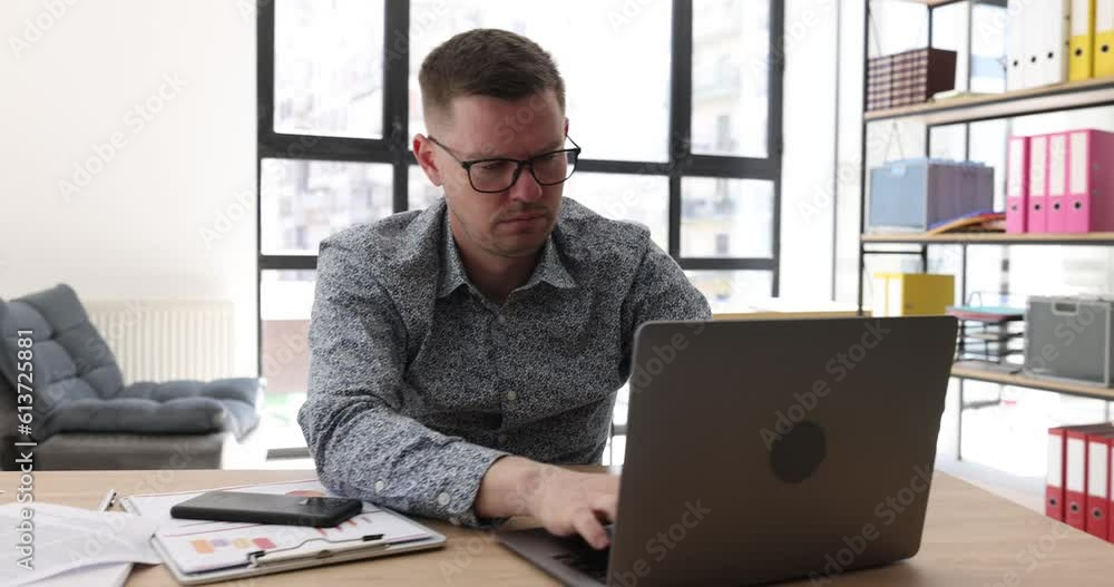 A sleepy business man in the office typing a laptop, a close-up. Drowsiness in the workplace, tracking