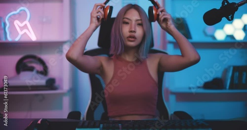 Footage of Young Asian female esports gamer sitting in chair facing back and looking at camera with neon lights at home. Female gamers are enjoying the technology of live streaming.