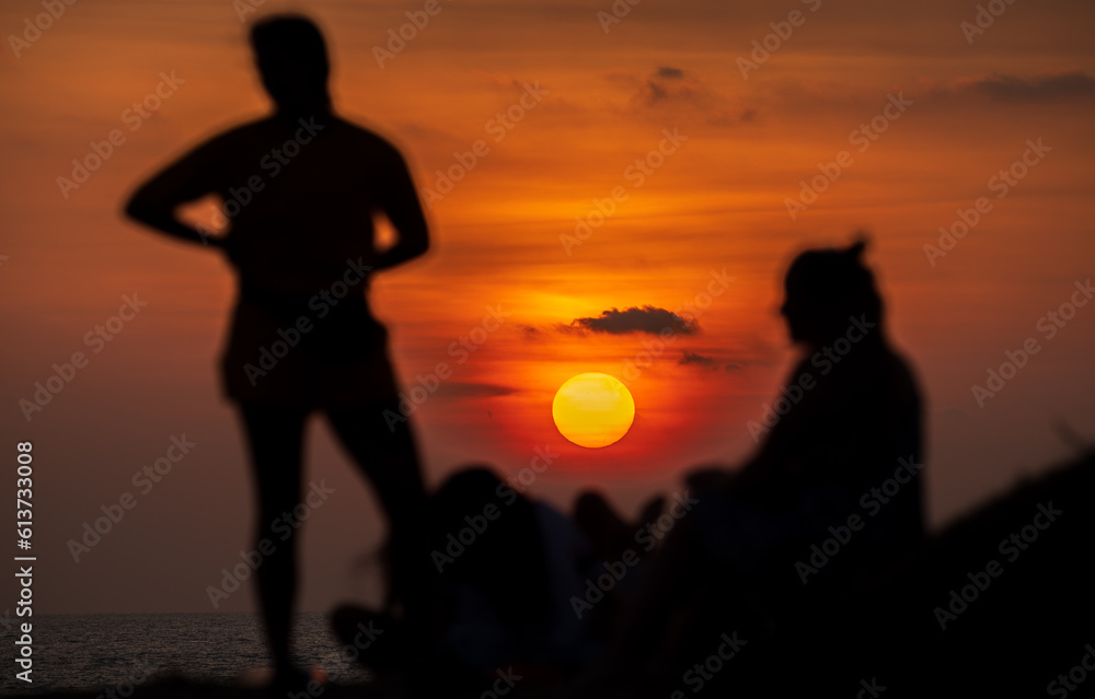 Enjoying the sunset view on the tropical beach in Galle. Silhouetted group of people in the foreground.
